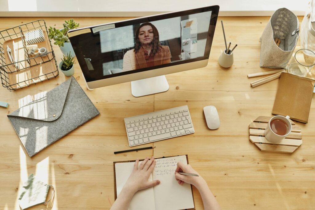 FAQ Person taking notes during a video call at a neatly organized home desk, showing remote work lifestyle.