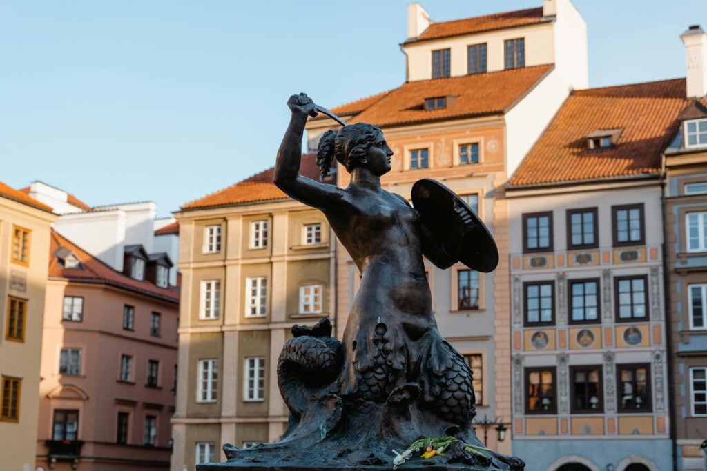 The iconic Syrenka statue in Warsaw's Old Town, representing the city's emblem under daylight.